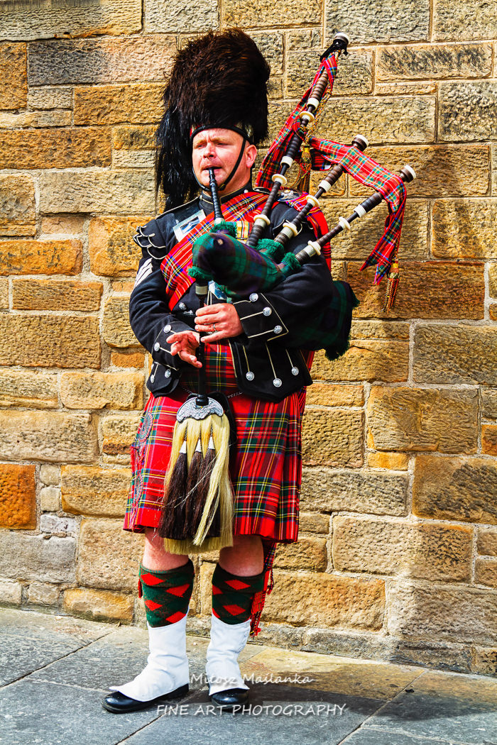 Scottish bagpiper dressed in traditional red and black tartan dress.