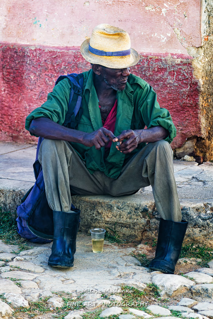A street portrait of an old cuban man, african carnation, who is sitting in relaxation and smoking his cigarette, calm,