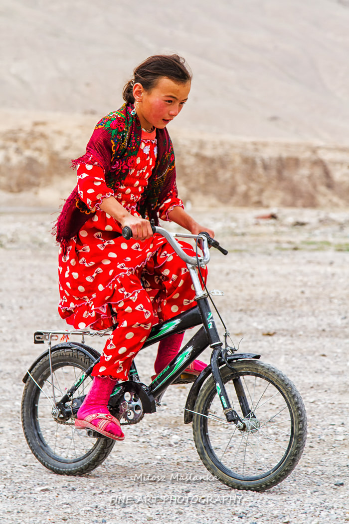 Little girl riding her bicycle in Pamir mountains. Pamir highway is part of a famous silk road.