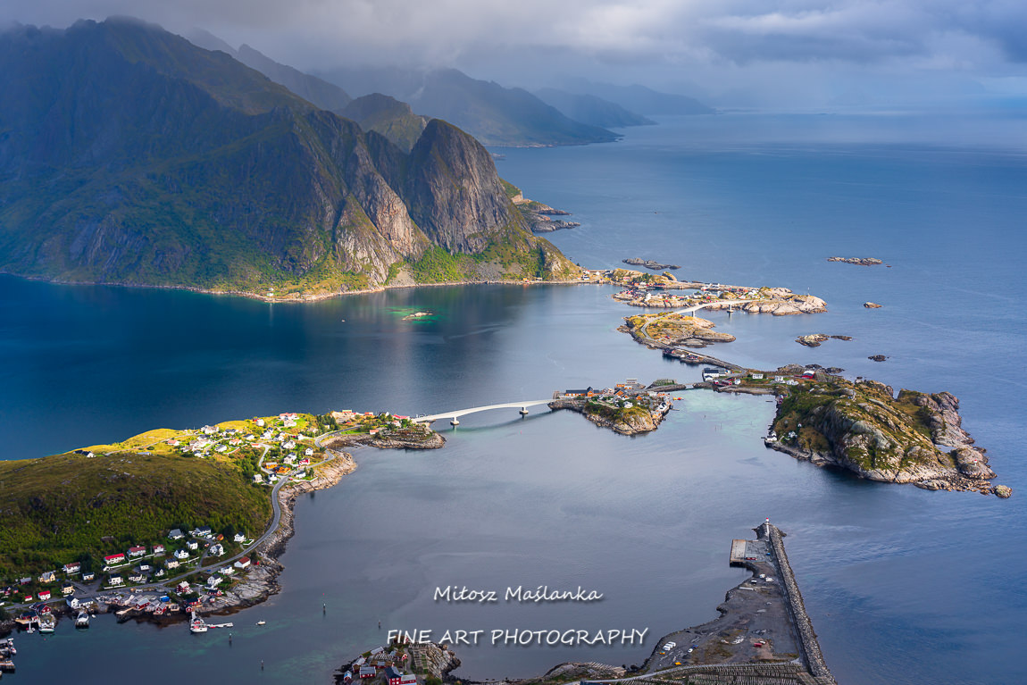 Sunny aerial panoramic view on stunning mountains and village of Reine in Lofoten islands, Norway from Reinebringen ridge. Scenic vista with a rainbow and rugged peaks.